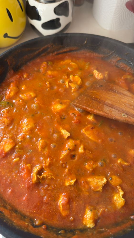 A saucepan full of chicken tikka masala is merrily simmering away over the heat. There’s a wooden spoon in the pan on the right. 