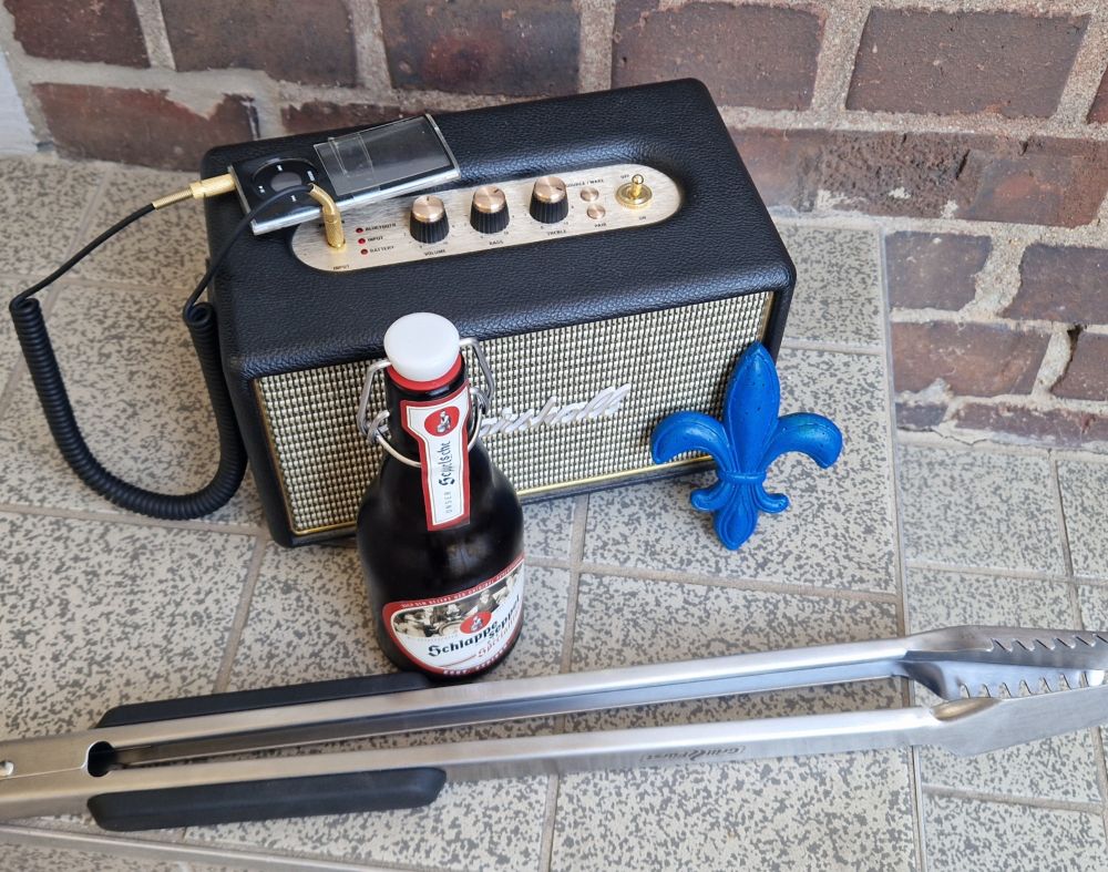 Eine Grillzange, eine Flasche Bier, eine Musikbox. Und eine Lilie.
