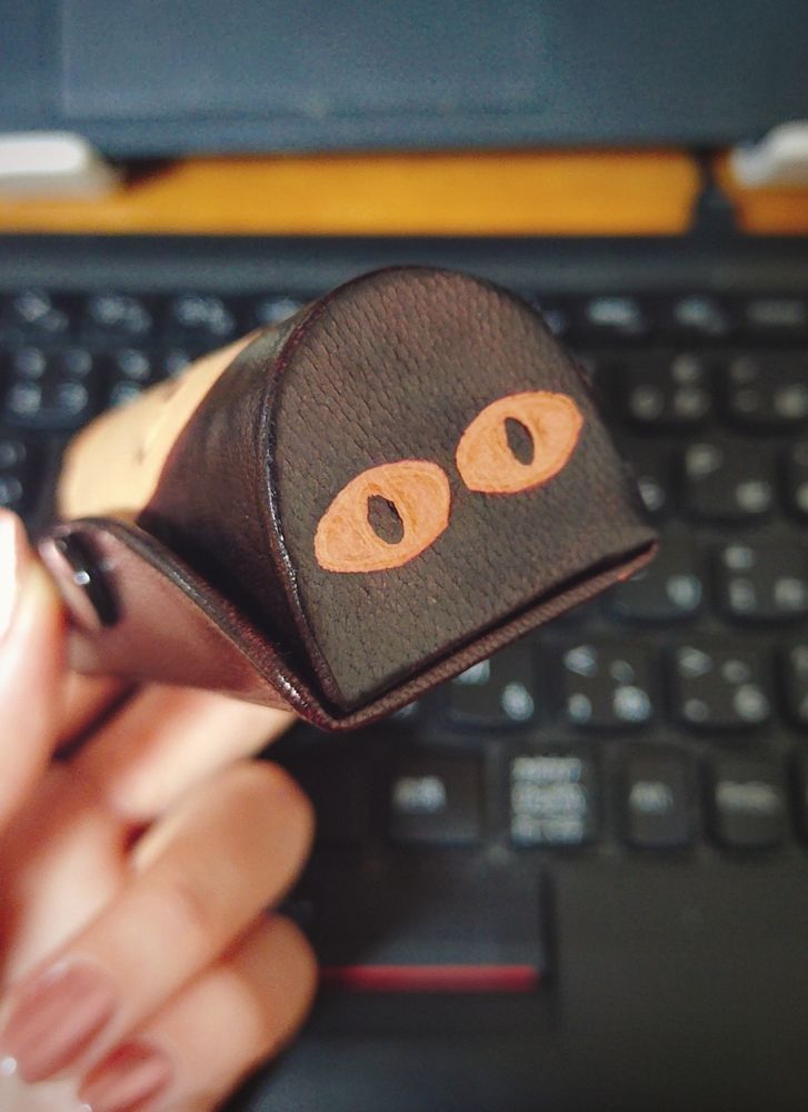 リップケースの写真。
左手でリップケースを持ち、側面が写っている。側面にメジェド様の顔が印刷されている。