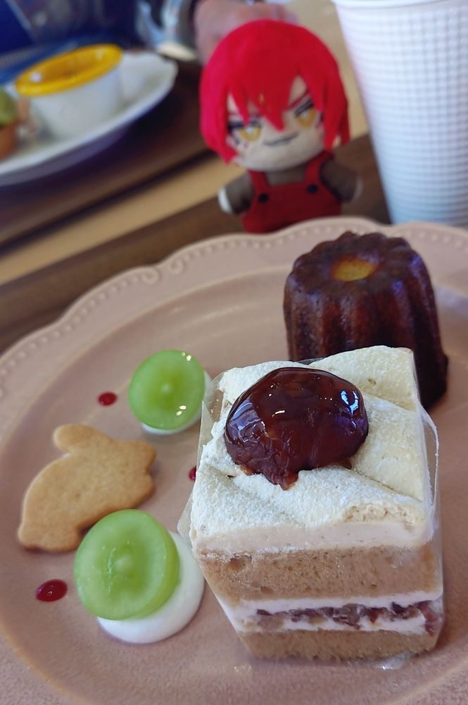 ぬいとケーキの写真。
左側にクッキーとシャインマスカットのカット、右側に栗ショートとカヌレ、奥に自作アシュぬいがある。