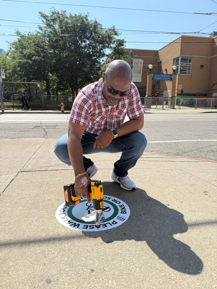 Toronto city councillor Chris Moise hot drying a sticker to the sidewalk