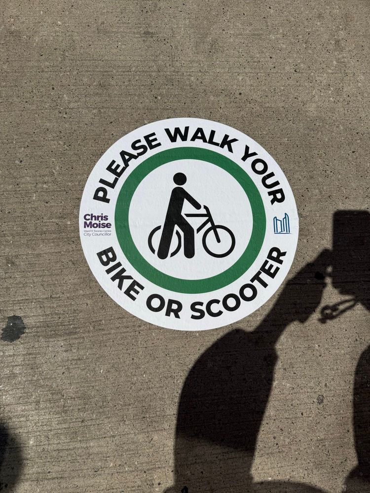 The sticker, which is round has a cyclist in the middle and is in circled with the words please walk your bike or scooter