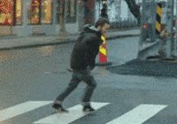 A person walking along a crosswalk as strong winds push back against them.