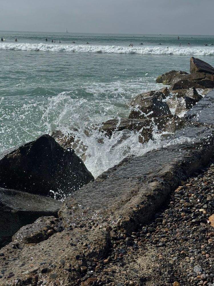 Waves splash on large rocks as the tide begins to come in at the beach.