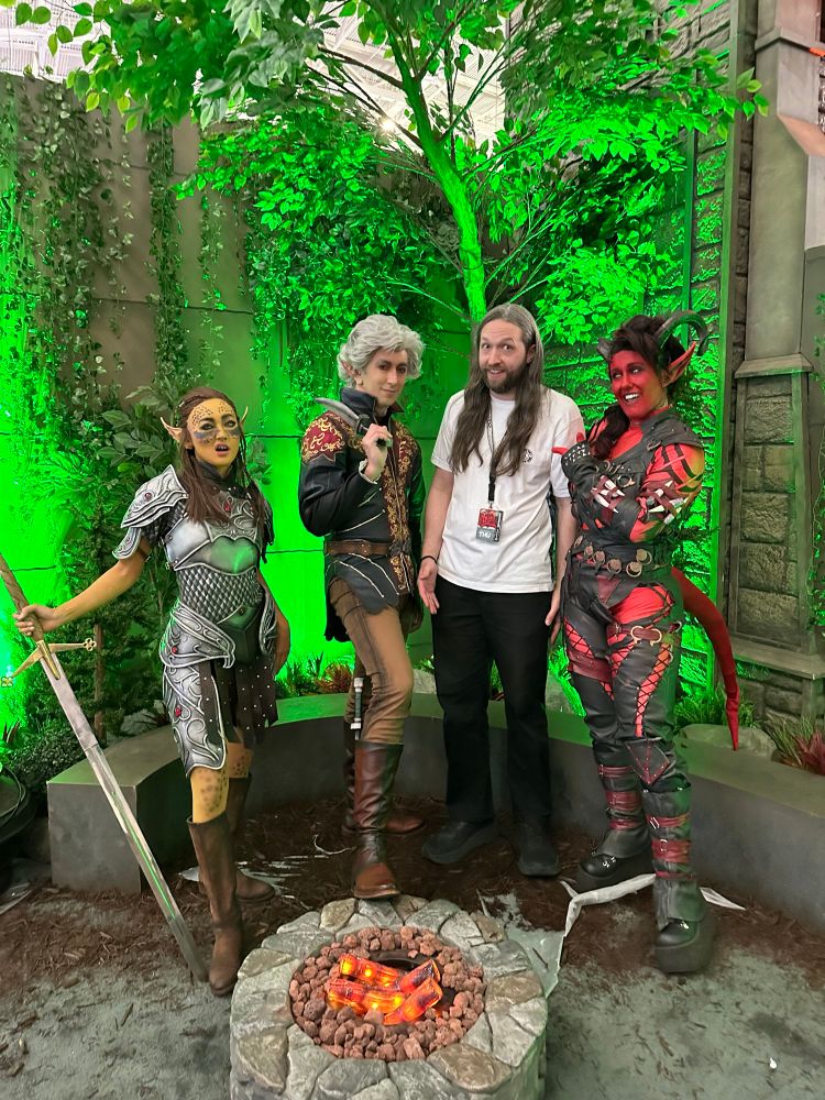 A guy with long hair stands at a Larian Studio Booth with Lazel Astarion, and Karlach at PAX East 2025.