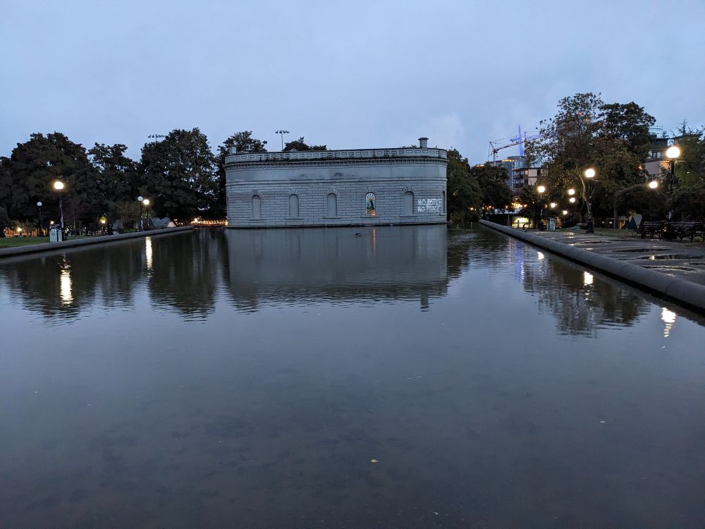 Across a large reservoir, St. Rat (community is our savior) is visible with a single candle in the dark rainy morning. 