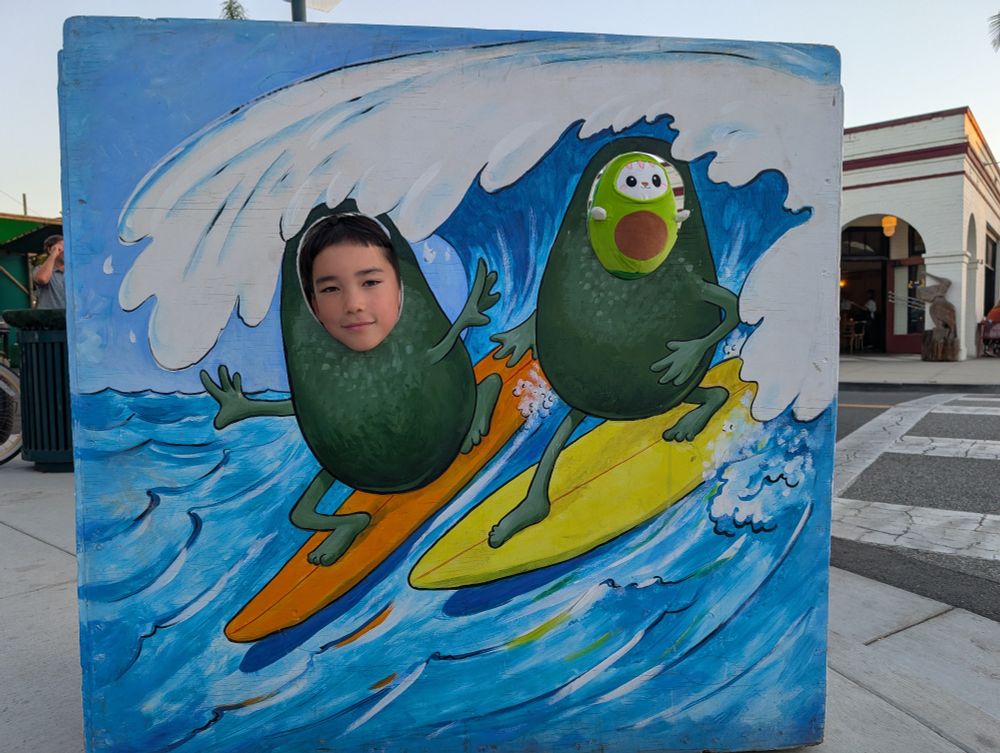 The kid being photographed in a face-in-hole board at the fair, near the newly-opened Linden Square. In one of the 2 holes is the "avocato" doll I'd just gotten for her, the one souvenir we really got this year (although we scoped out some stuff we'll likely get next Saturday/11th at the Oxnard Day of the Dead celebration —happening on such an early date, yes, from 1-8pm!)