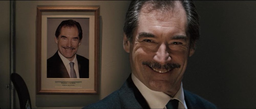 Timothy Dalton as supermarket owner Simon Skinner in HOT FUZZ smiling in front of a framed picture of himself wearing the exact same smile