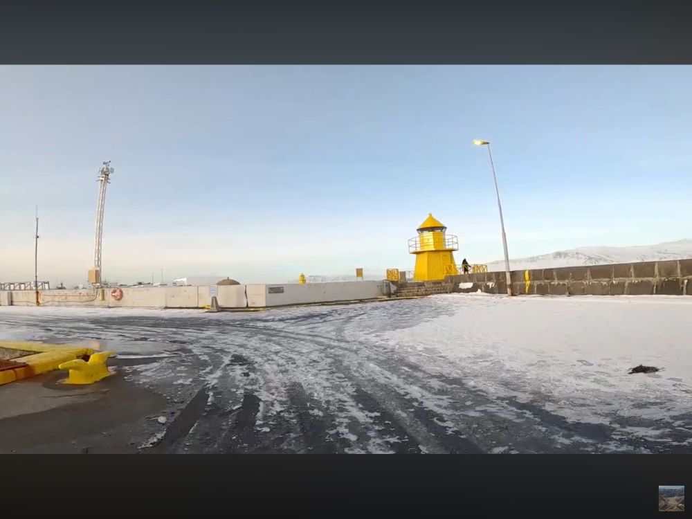 Concrete pathway with snow and ice leading to a yellow metal lighthouse approx 5m tall on a harbour wall in Reykjavik Iceland