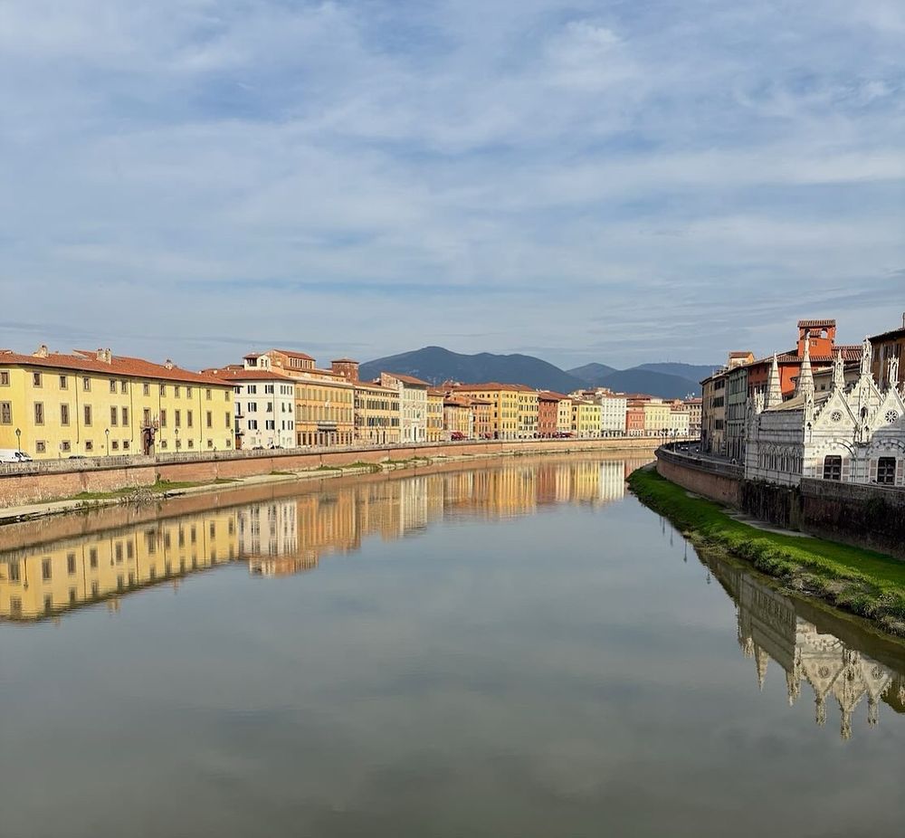 Buildings along the river Arno in Pisa with reflections in the water. 