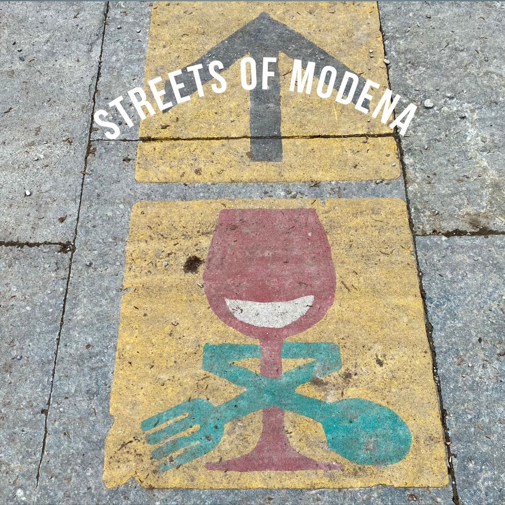 Painting of smiling wine glass on a sidewalk in Modena, Italy.