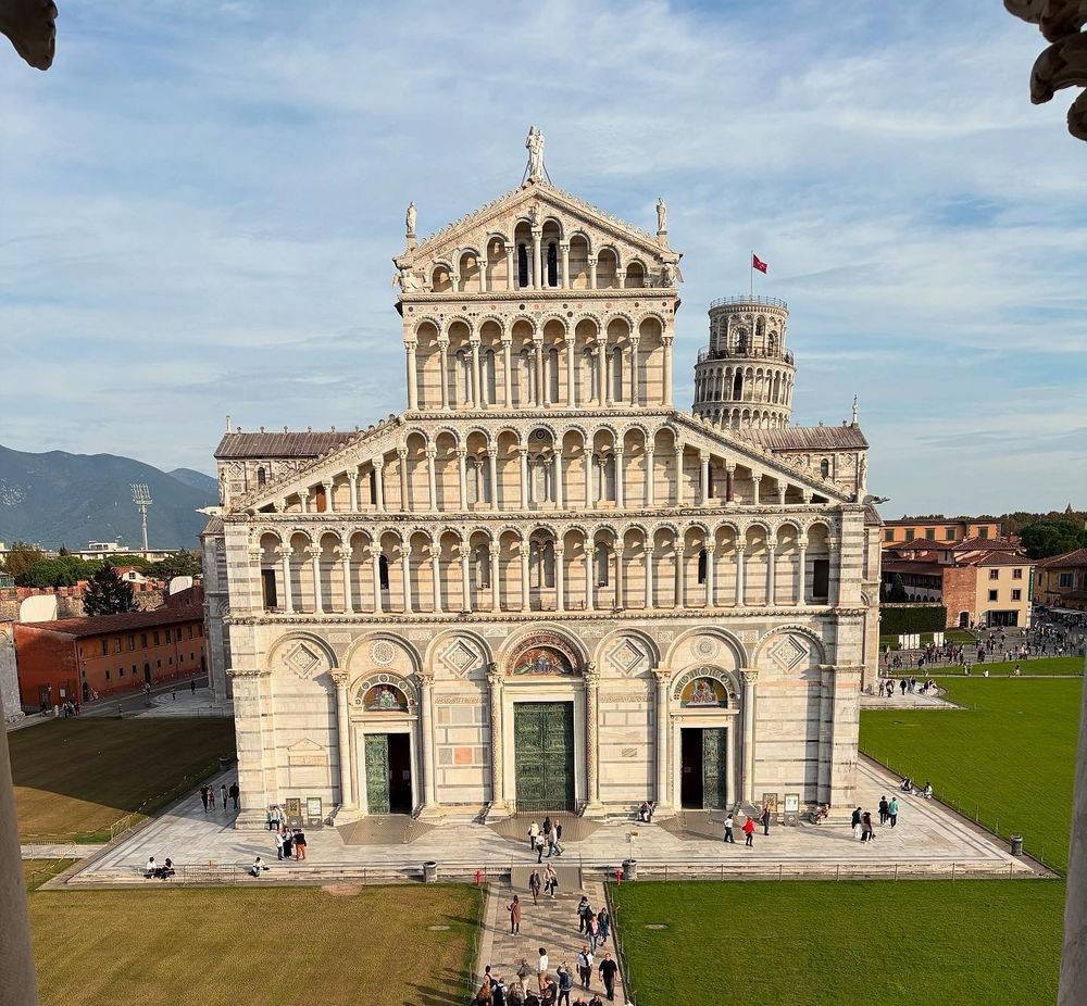 The facade of the white duomo against green grass. 