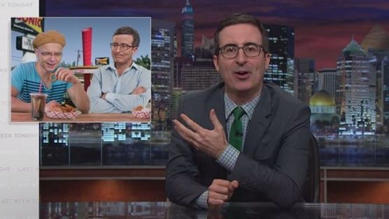 John Oliver gesturing to a graphic of John Oliver at a Sonic restaurant with another person.