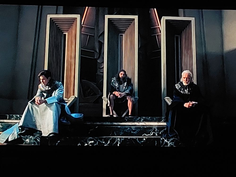 Photo of a scene from Season 3, Episode 3 of the 'Foundation' TV show in which the characters Dawn and Dusk sit on the throne room stairs with Day behind them sitting on the middle throne.