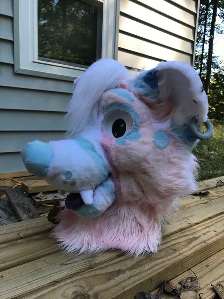 Fursuit head of a pink dog with blue accents.