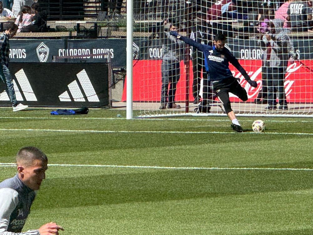 Goalkeeper kicking a ball in warmups in front of the goal.