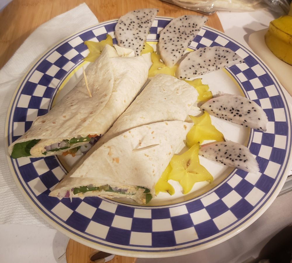 A spicy wrap on a plate with fruit.