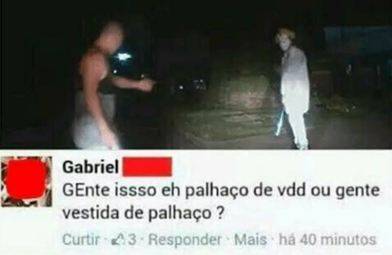 print do facebook. vemos a foto de um homem de frente para outro, que está vestido de palhaço. a imagem é em um lugar escuro e pouco nítido.  embaixo dela, o comentário: "Gente issso eh palhaço de vdd ou gente vestida de palhaço ?"