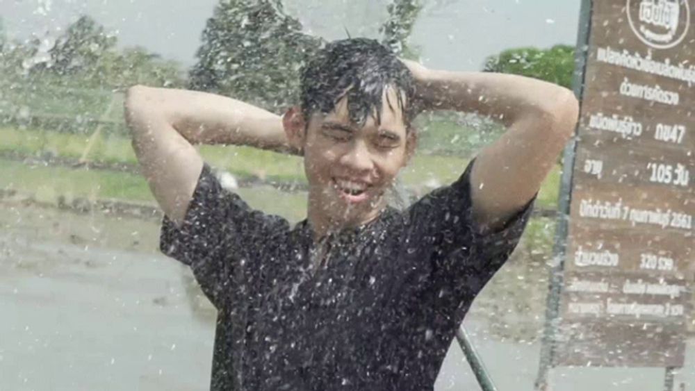 a man in a black shirt is standing in the rain with a sign in the background that says ' thailand ' on it