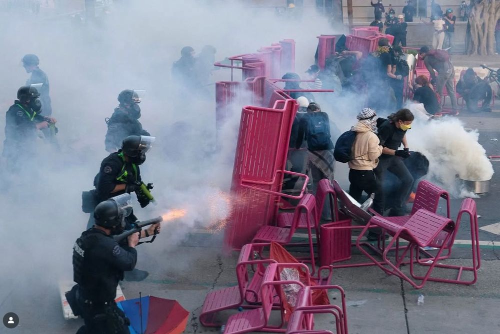 Hot pink chairs and benches stacked up in a protest with protesters hiding behind them as law enforcement fires upon the barricades with rubber bullets and tear gas 