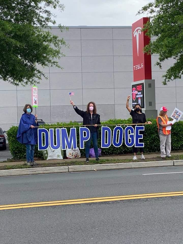 Activists hold sign DUMP DOGE at Tesla