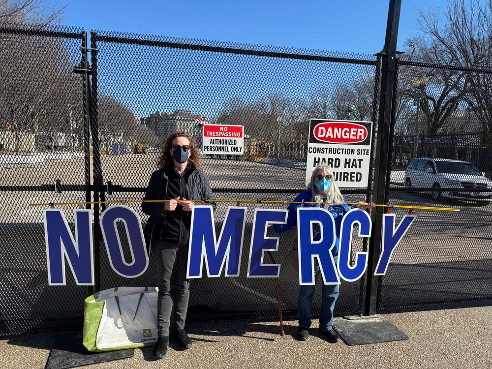 Activists hold sign NO MERCY at fenced in White House