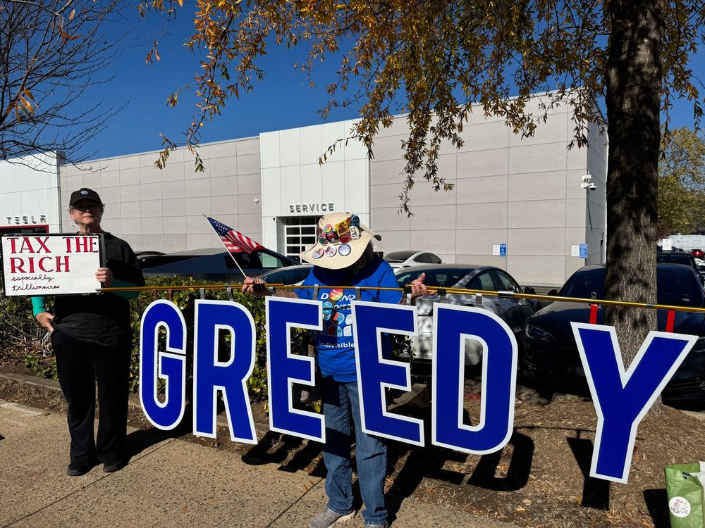 Activists hold sign GREEDY and Tax The Rich especially Trillionaires
