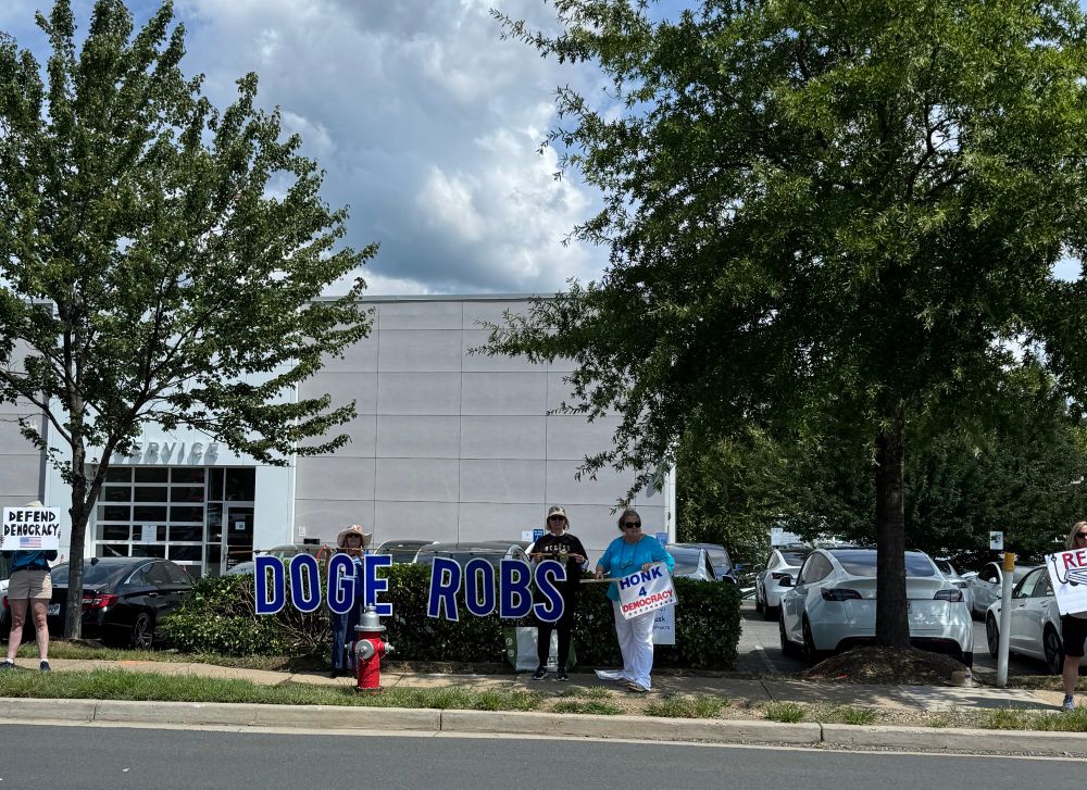 Activists hold sign DOGE ROBS at Tesla