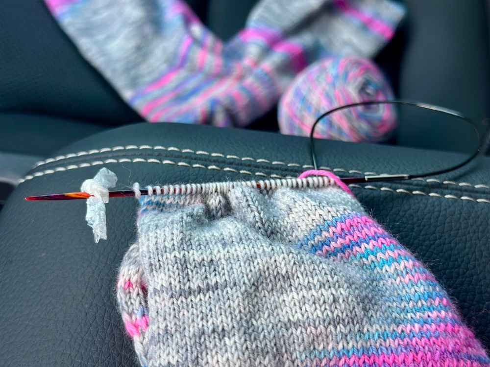A pair of socks are being knit, with a candy wrapper saving the day by marking the beginning of a new row. 