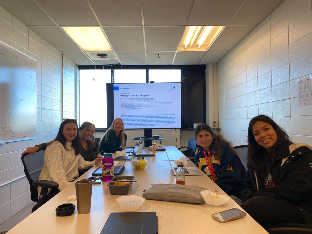 A group of enthusiastic virology trainees sitting around a table discussing a journal article recently published in Cell titled “Virology - The next 50 years”