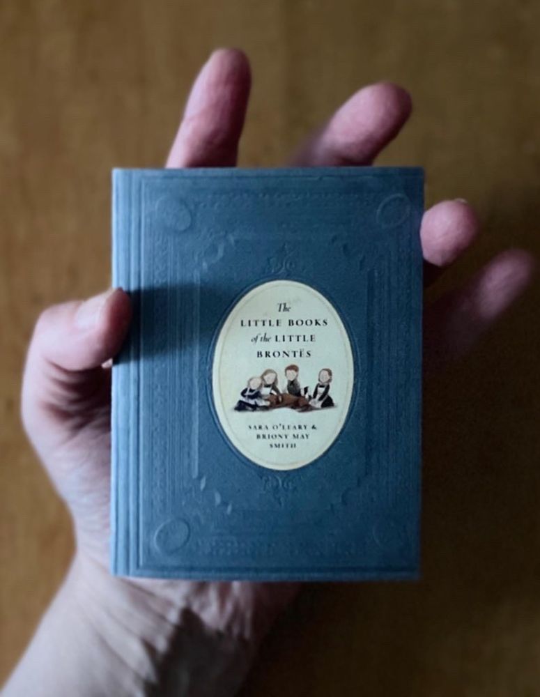 Hand holding small blue book with cameo inset reading The Little Books of the Little Brontës