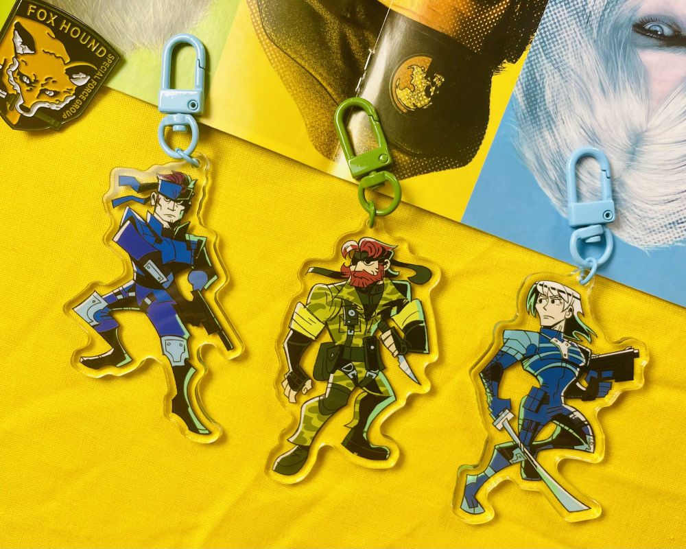 Photo of a set of MGS character charms on a yellow background. 