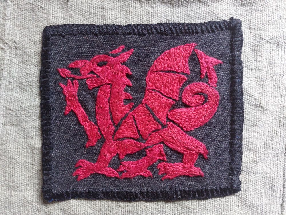An embroidered patch showing a red dragon in the style of the Welsh flag, on a background of grey denim