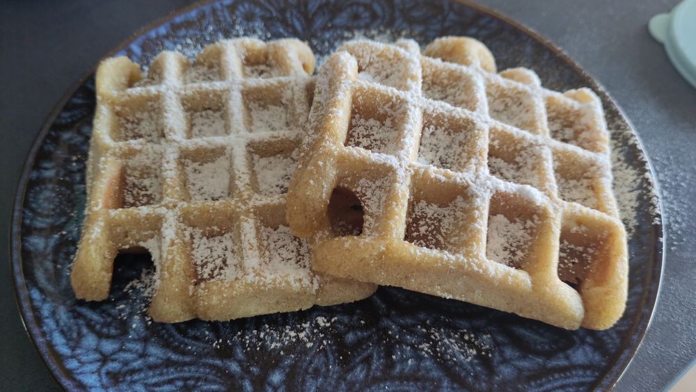 Zwei belgische Waffeln mit Puderzucker auf einem blau gemusterten Teller
