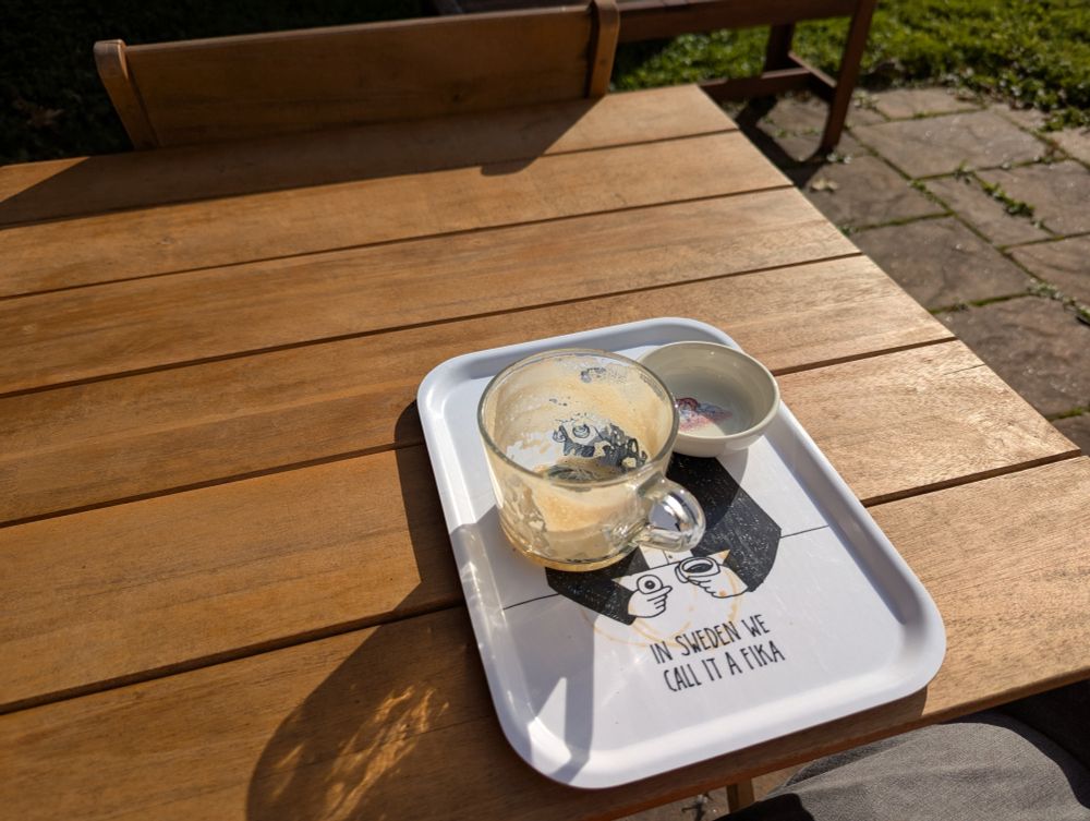 The same scene, except the mug is empty other than some foamy film, the bowl has only crumbs, and the tray has a few visible coffee rings.