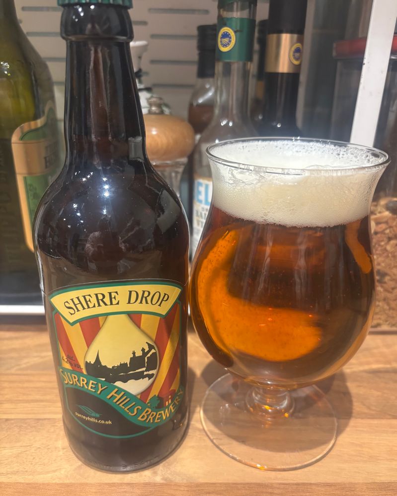 A bottle of beer with a silhouette of a town scene and the name Shere Drop next to a glass filled with that beer