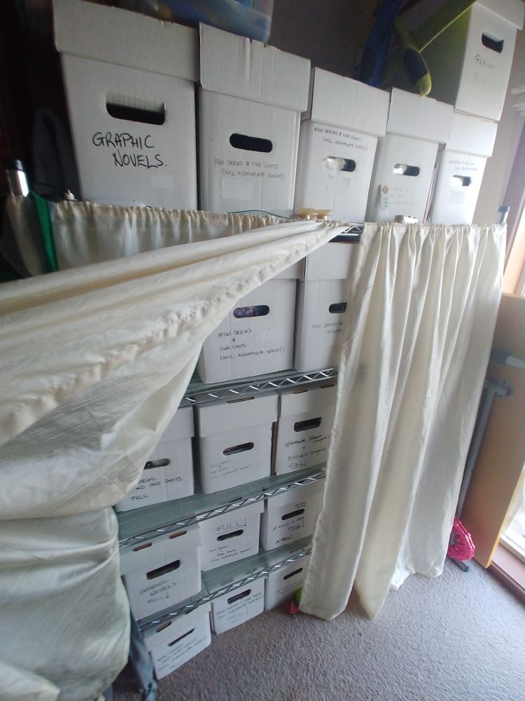 Lots of comic boxes stacked on some shelves with a curtain partially covering them.
