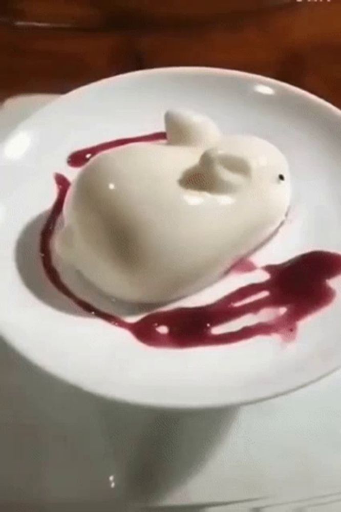 a white plate topped with a white dessert in the shape of a rabbit covered in red sauce .