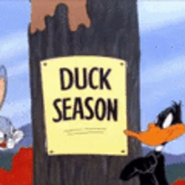 a sign that says duck season is next to a tree