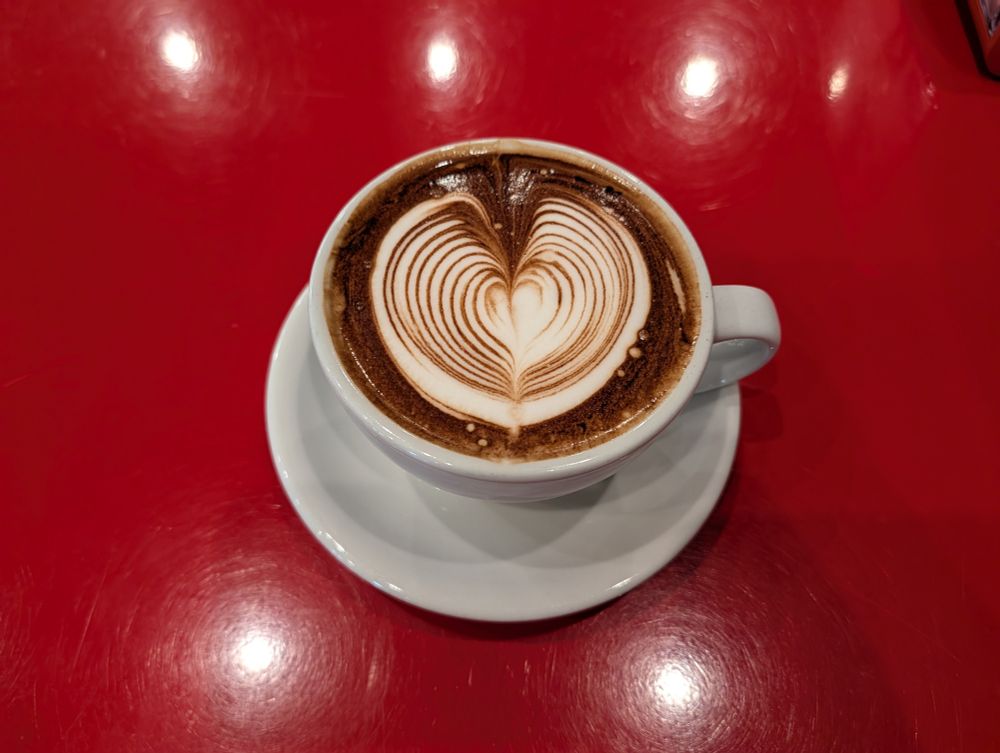 A mocha latte with heart shaped foam in a white cup on a red table.