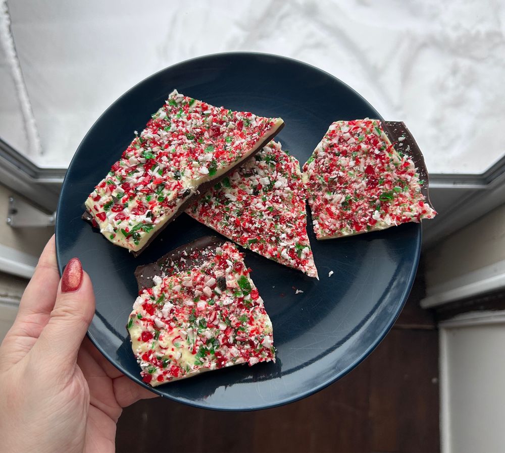 I’m holding a plate of peppermint bark - shards of candy canes embedded in a layer of white chocolate on top of a dark chocolate base.