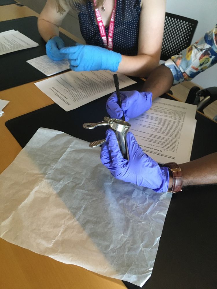 des étudiant-es, assis autour d'une table, dont on ne voit que les bras et mains gantées, manipulent et examinent un speculum à bec de canard. ils utilisent une liste de question pour faire parler l'objet et prennent des notes.