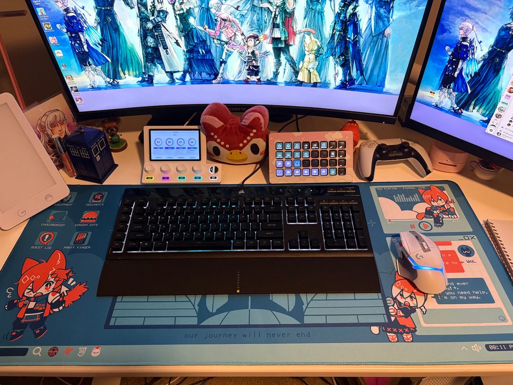 Keyboard mouse mat with various cute drawing of a red haired cat boy. Monitors and various nerd things are scattered in the background. 