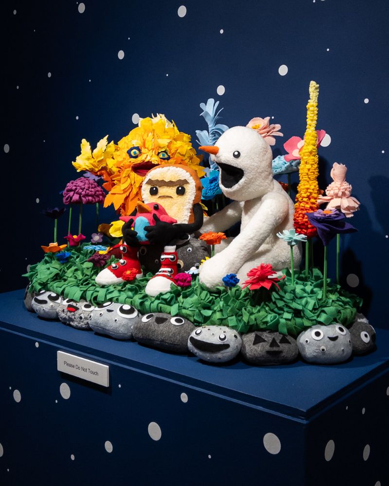 A family of imaginative characters of felt and fiber—including a fireball, a snow person, a grumpy piece of toast, and a gumdrop penguin—sit in a garden of vibrant flowers and potato rocks.

Image credit: JooYoung Choi, The Freizor-Bern Family: And it was Plain to See You were my Destiny, 2019-2025, wooden armature, quilt poly fiber batting, fleece, poly-fill, metal hardware, polyfoam, and felt. Courtesy of the artist and Inman Gallery.
