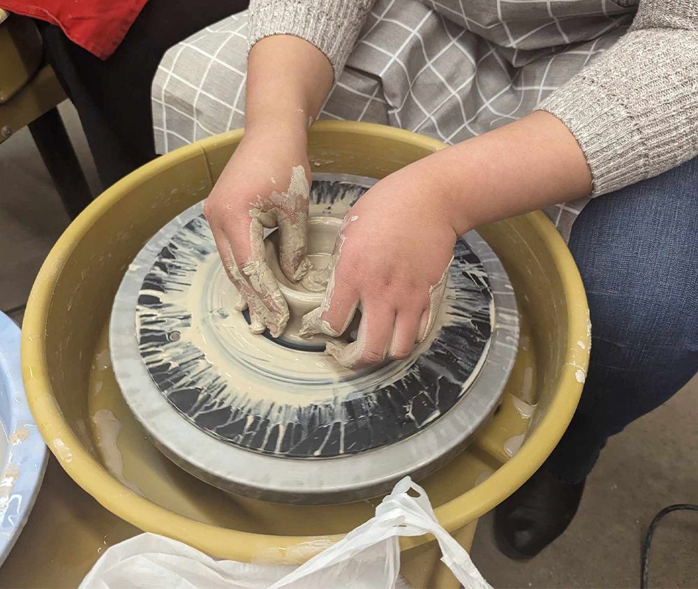 A person sits at a pottery wheel, shaping clay into a bowl shape.