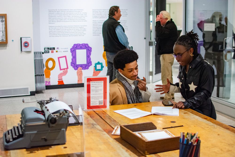 Two people discuss the Sourced from the Zoo object guide while kneeling at a table with a typewriter on it.