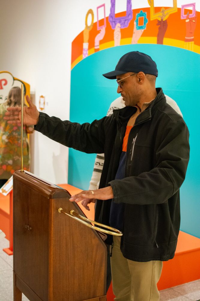 A person wearing a black jacket and hat operates a theremin, a musical instrument contained in a wooden cabinet with metal piping extending from it.