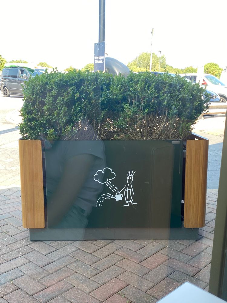 an outdoor planter. the picture on it shows a raincloud raining into a man's watering can, which he then pours onto the ground. he is entirely superfluous to this process.