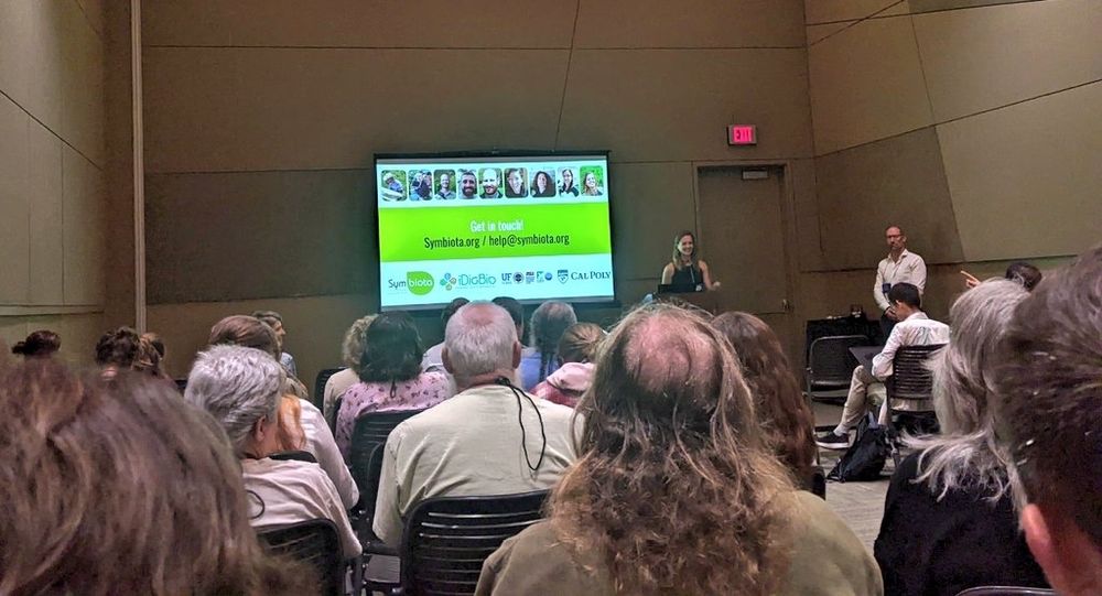 Presentation room with slide in background, colored green and white. The foreground is of the audience.