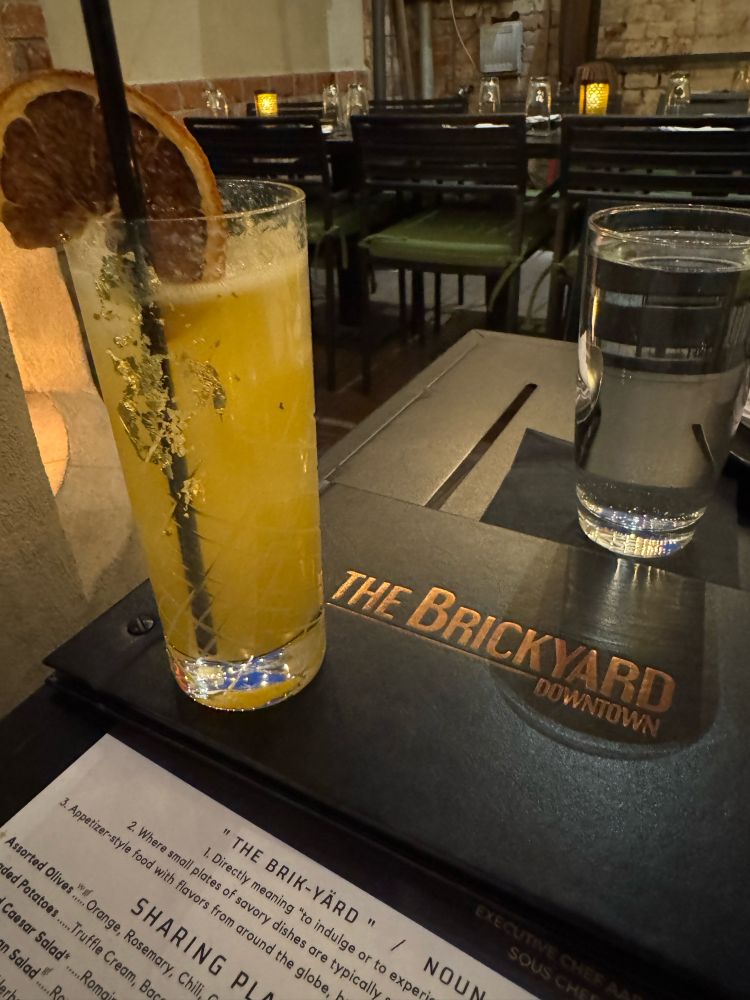 Cocktail in a tall glass, garnished with a dried blood orange and gold leaf on the side of the glass.